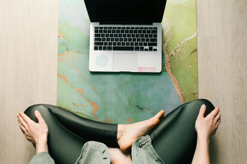 Woman sitting on a yoga mat in front of a laptop